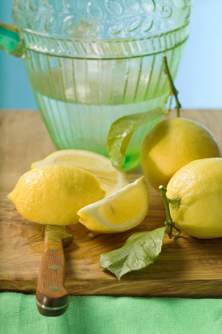 Frische Zitronen mit Blättern vor Wasserkrug