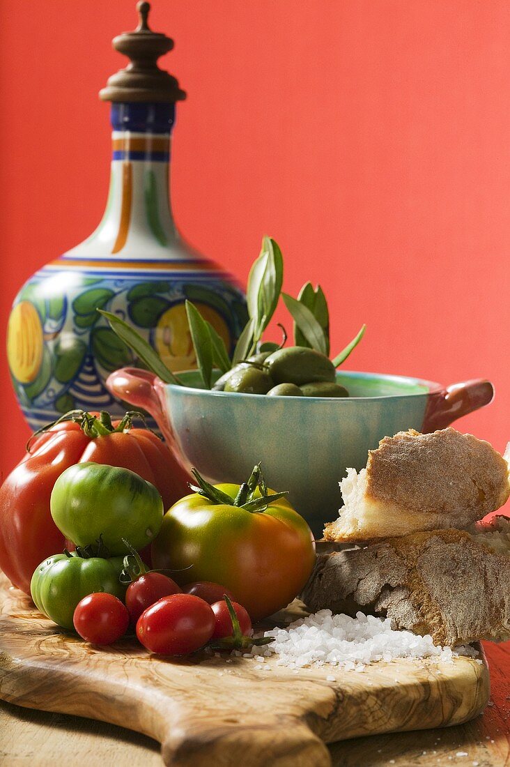 Frische Tomaten, Oliven, Brot, Salz und Keramikkrug