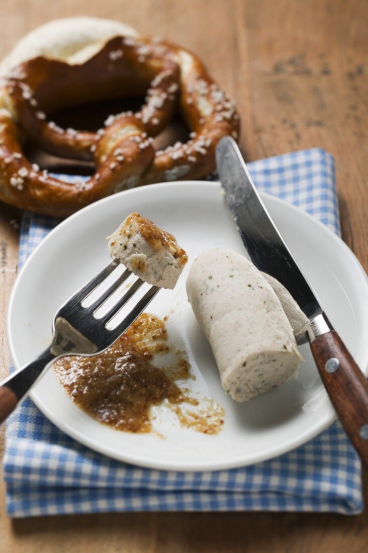 Cooked Weisswurst with mustard on plate, pretzel behind