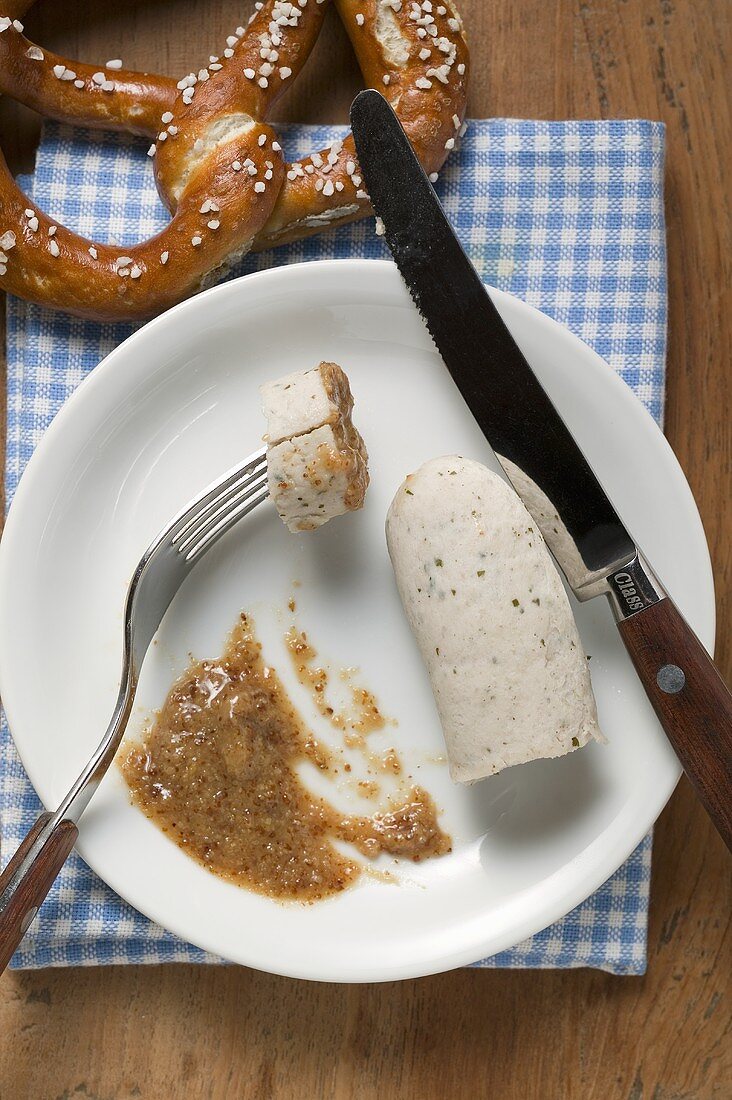 Gekochte Weisswurst mit Senf auf Teller, dahinter Brezel