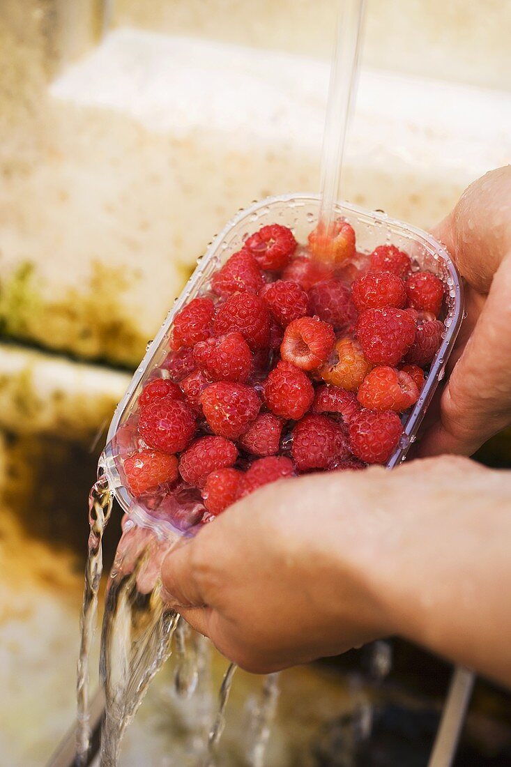 Hände halten Schale mit Himbeeren unter Wasserstrahl