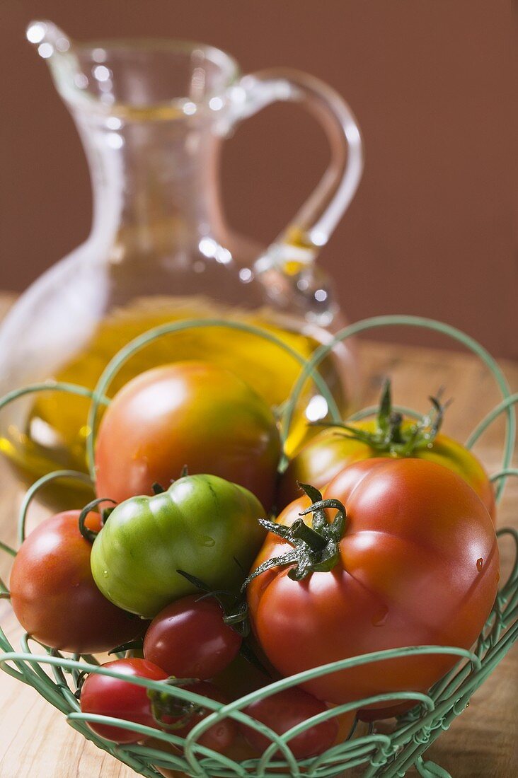 Assorted tomatoes in wire basket in front of olive oil