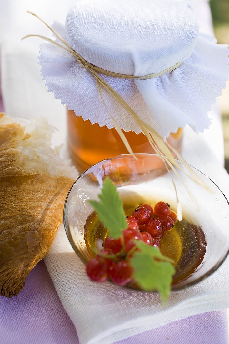 Honig, rote Johannisbeeren und Croissant auf Tisch im Freien
