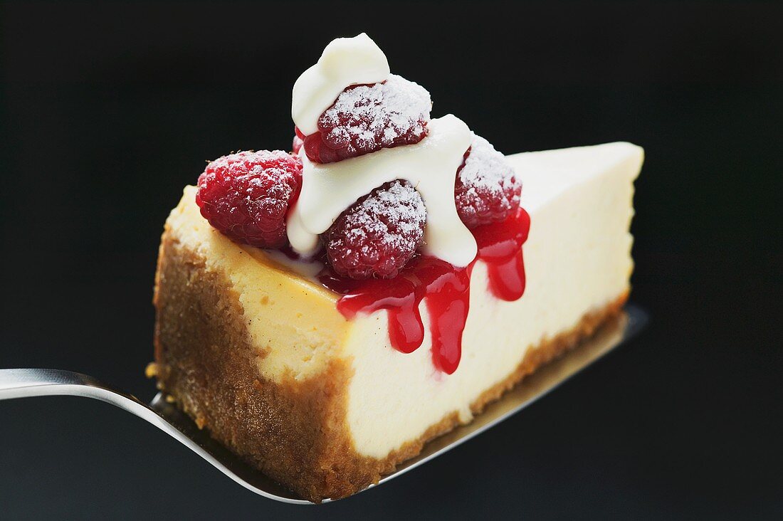 Stück Käsekuchen mit Himbeeren, Sahne, Puderzucker auf Heber