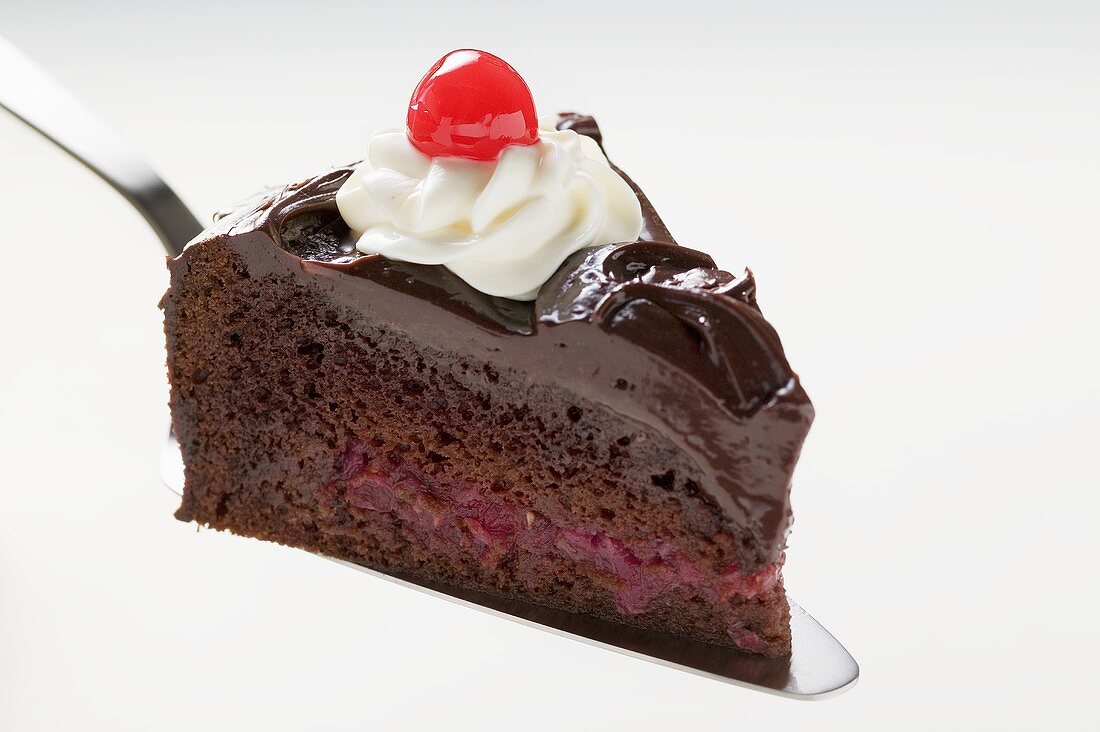 Slice of chocolate cake with cream & cherry on cake server