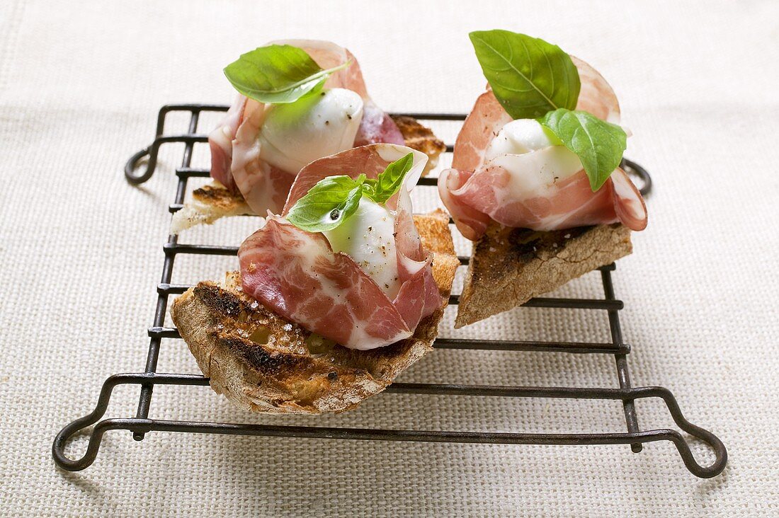 Drei Crostini mit Parmaschinken, Mozzarella und Basilikum