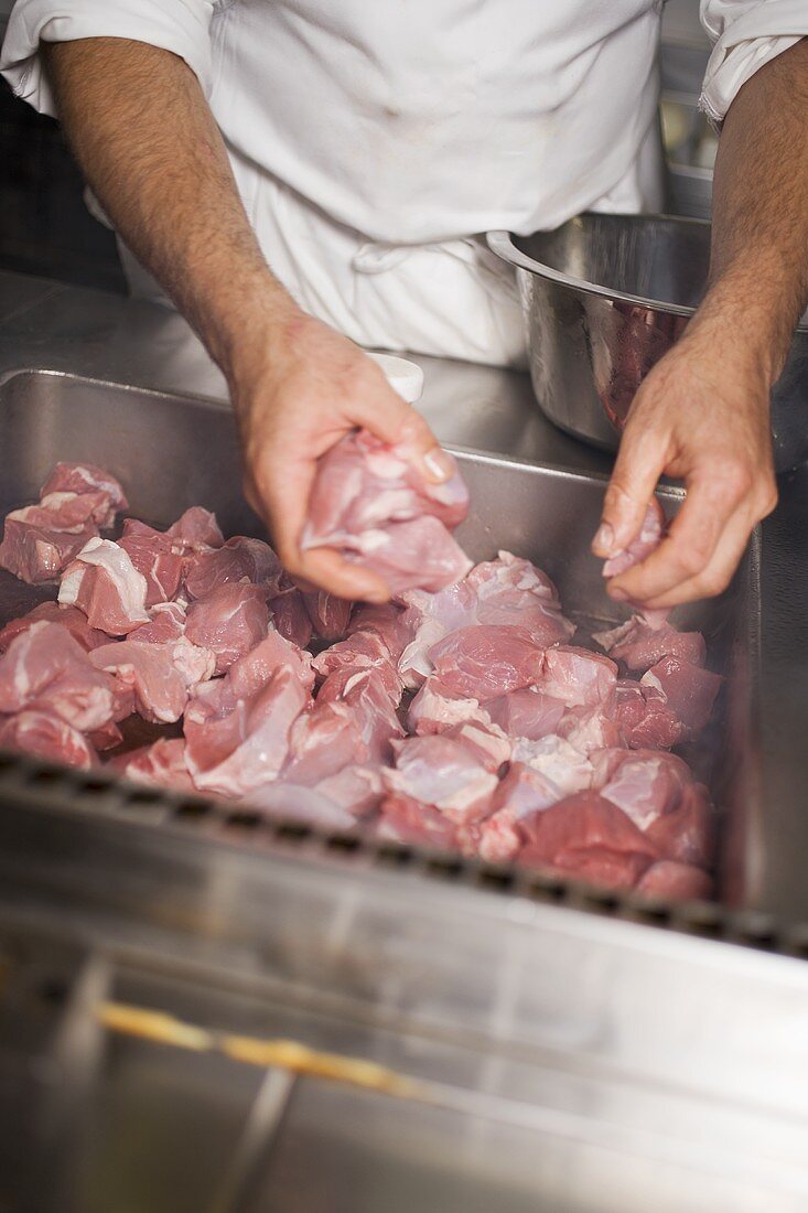 Koch verteilt Schweinefleisch in grosser Bratreine