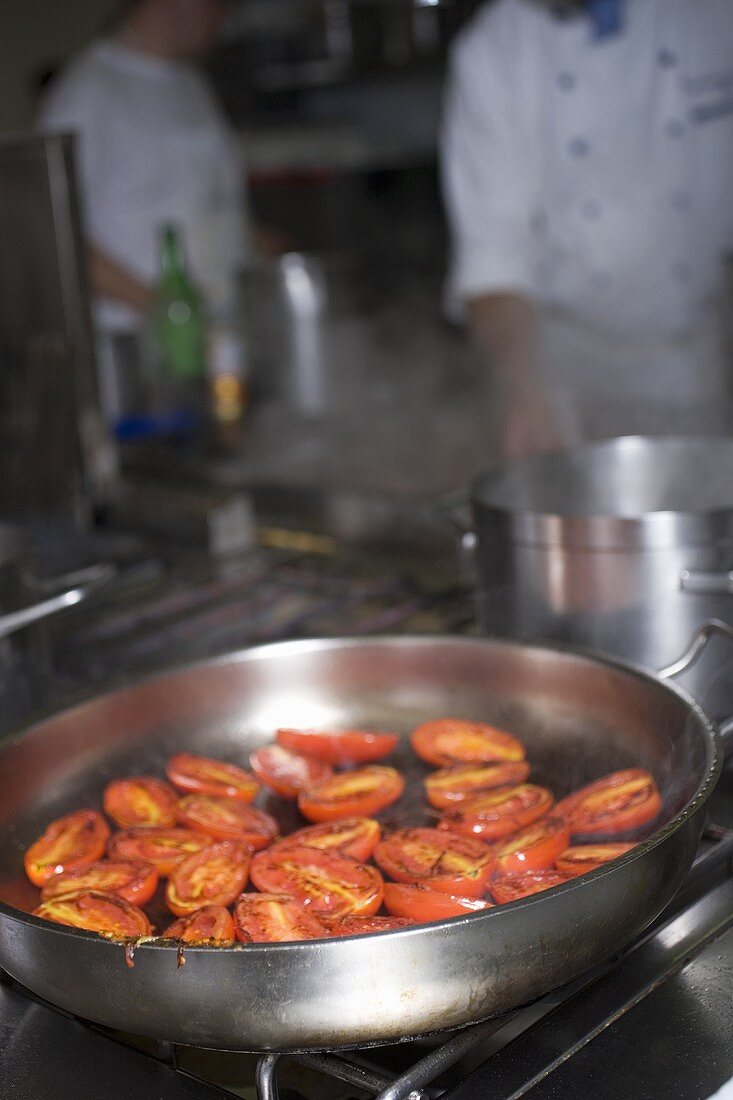 Tomaten in Bratpfanne auf dem Herd, Köche im Hintergrund