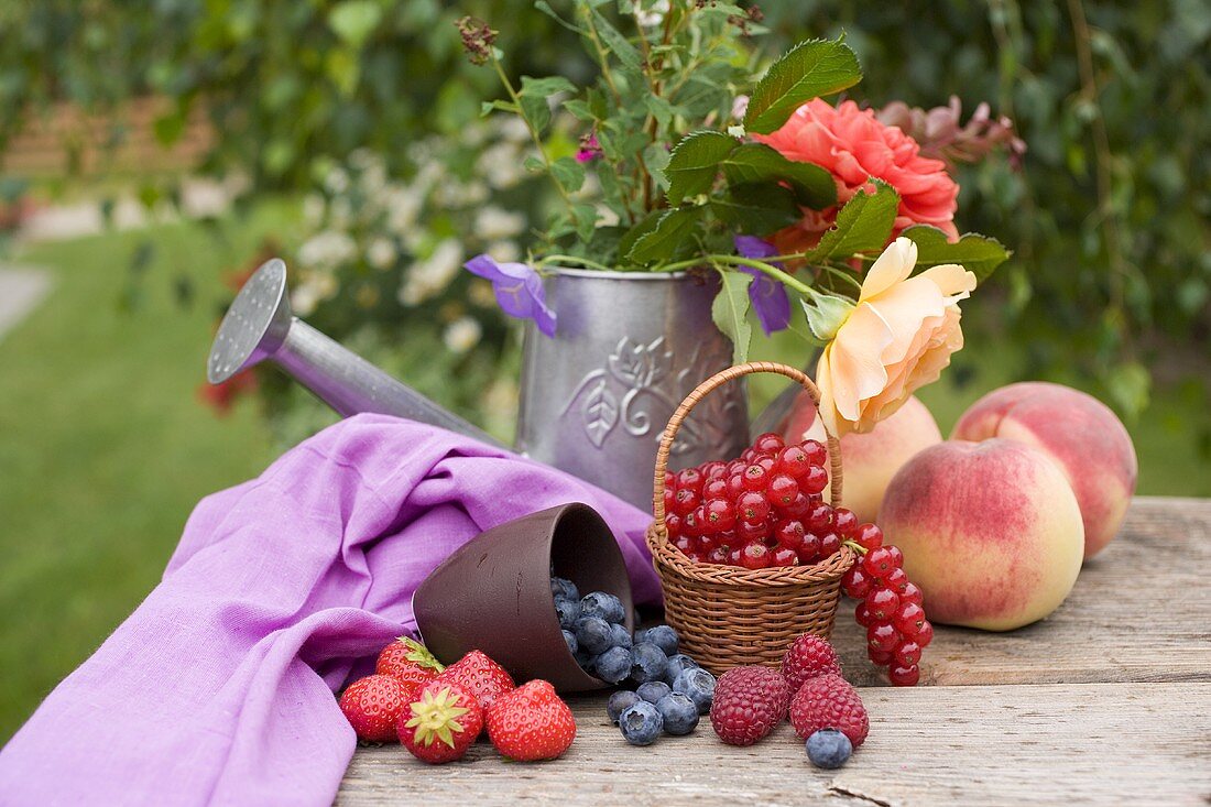 Pfirsiche, Beeren und Sommerblumen auf Tisch im Garten