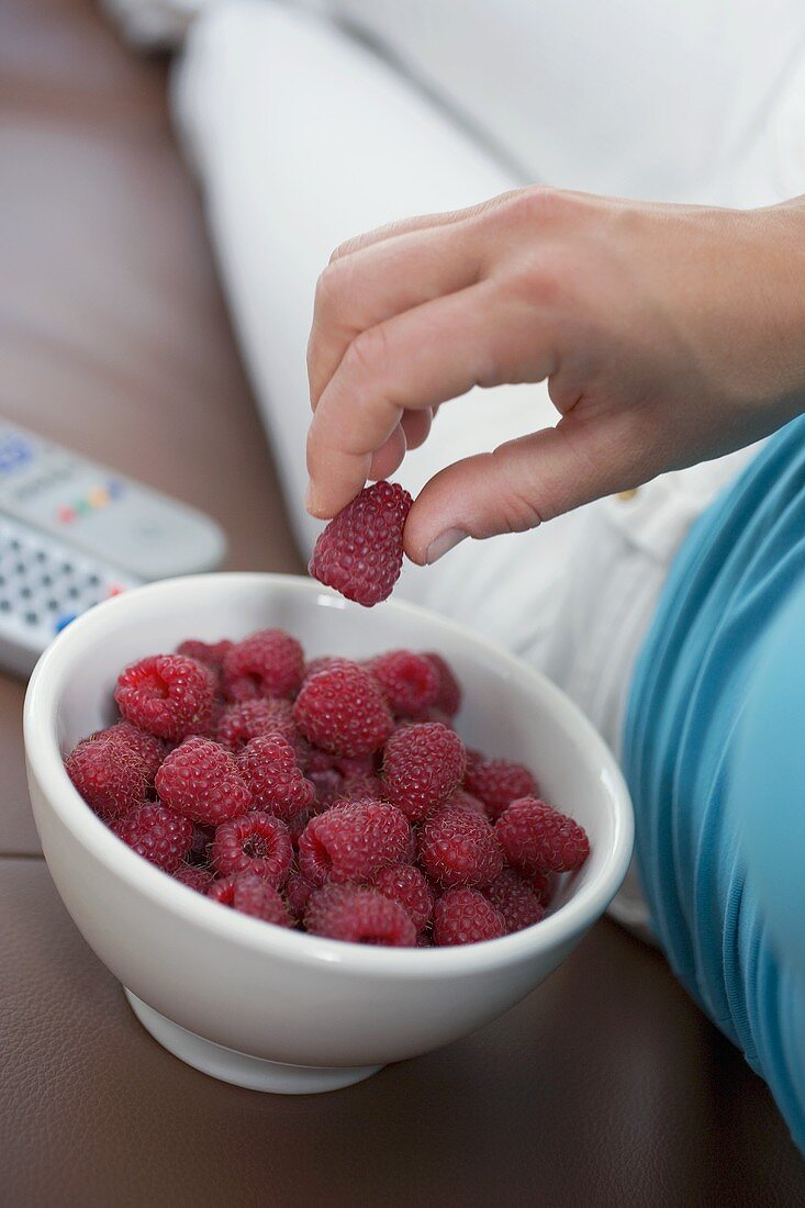 Woman watching TV eating fresh raspberries