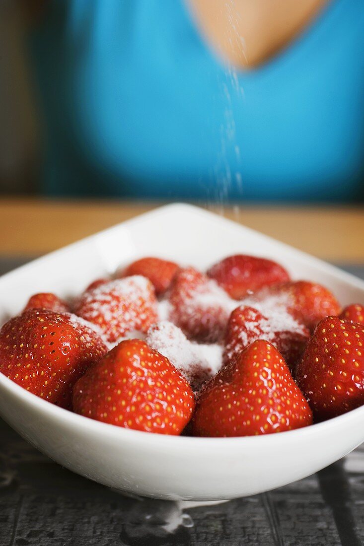 Sprinkling sugar on strawberries in white bowl