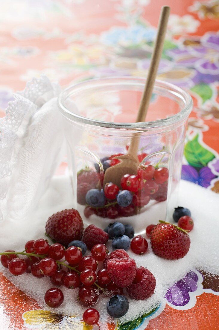 Fresh berries in jam jar with sugar and wooden spoon