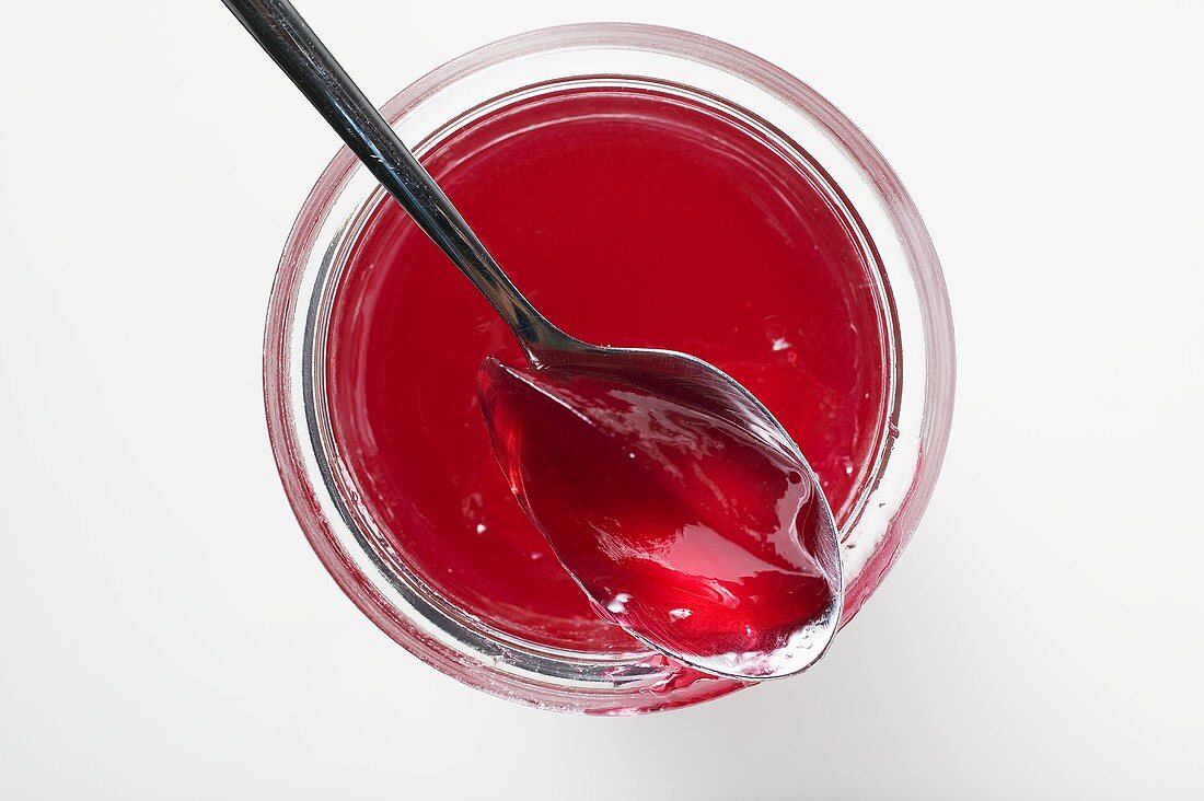A jar of redcurrant jelly, opened, with spoon