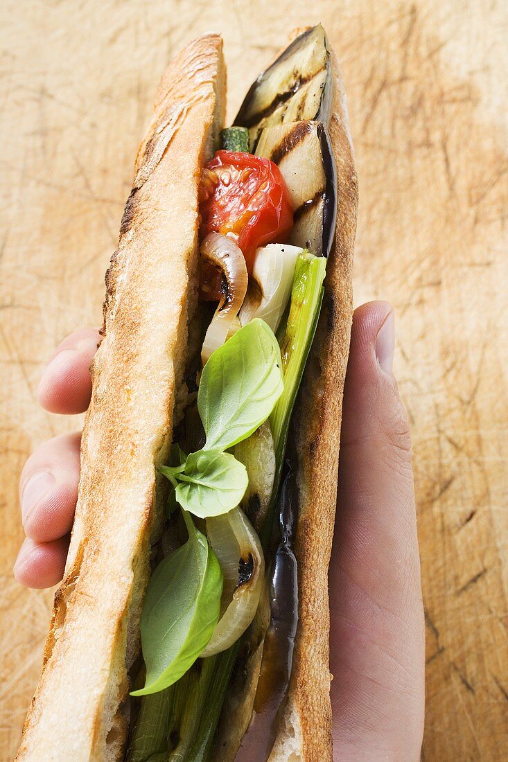 Hand holding grilled vegetables and basil in baguette