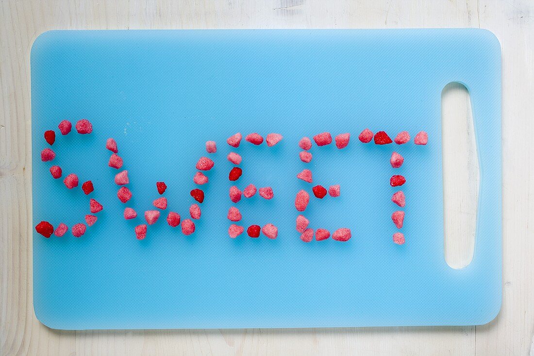 Schriftzug 'Sweet' aus Zuckerbonbons auf blauem Schneidebrett