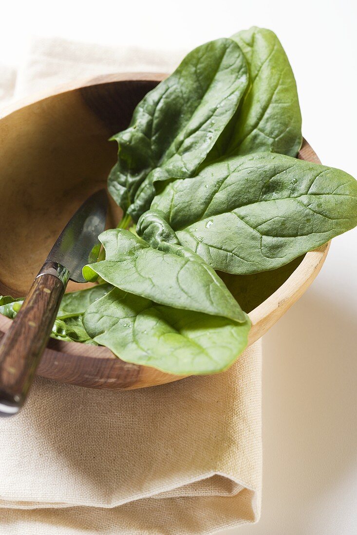 Several spinach leaves in wooden bowl with knife