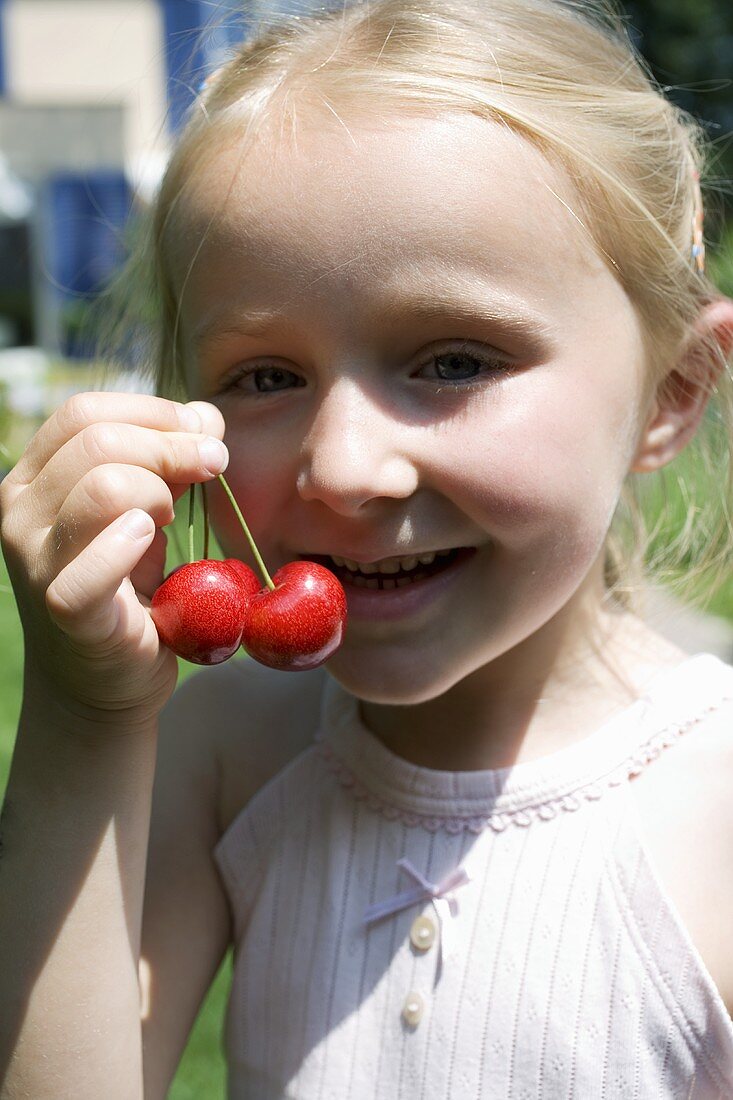 Blond girl holding a pair of cherries