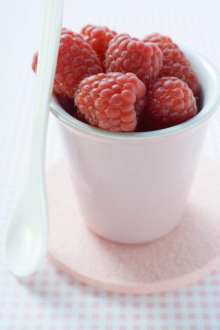 Himbeeren im Keramikbecher, daneben Löffel