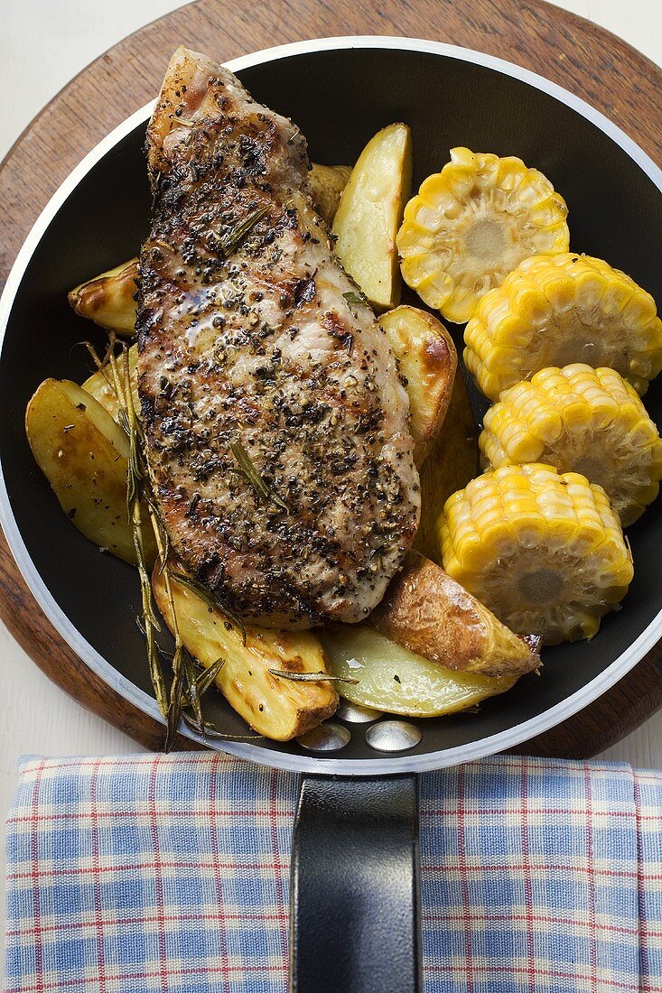 Schweinekotelett mit Bratkartoffeln und Mais in Pfanne