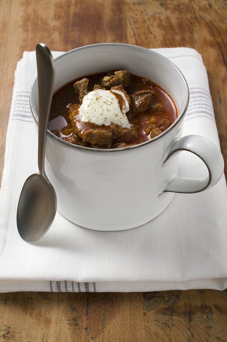 Gulaschsuppe mit saurer Sahne in Tasse, daneben Löffel