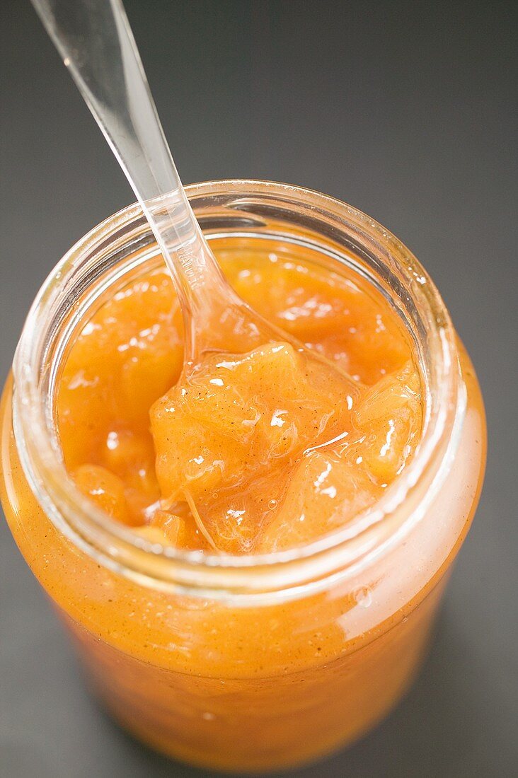 Ein Glas Aprikosenmarmelade, geöffnet, mit Löffel
