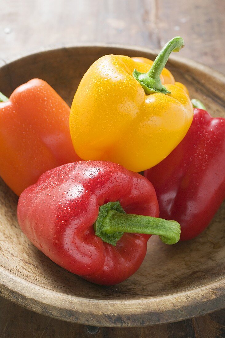 Mixed peppers with drops of water in wooden bowl