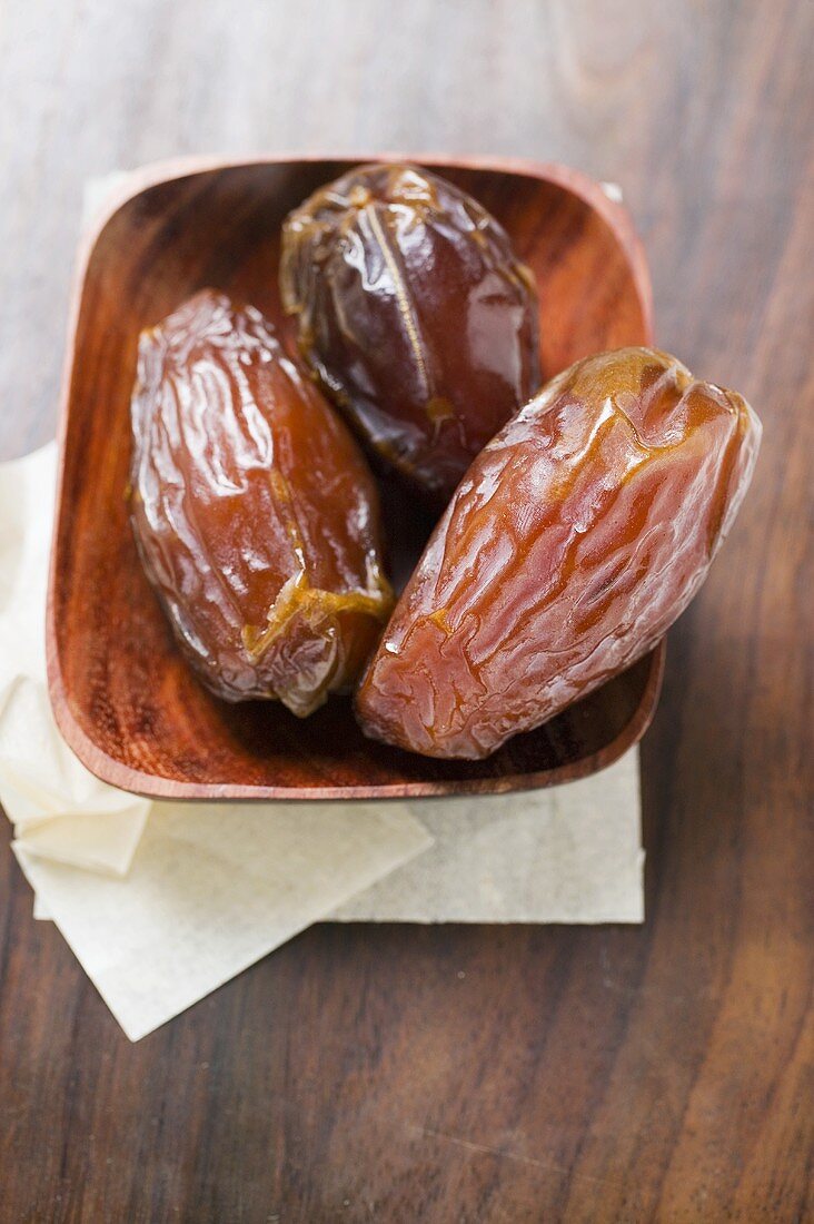 Three dried dates in wooden bowl