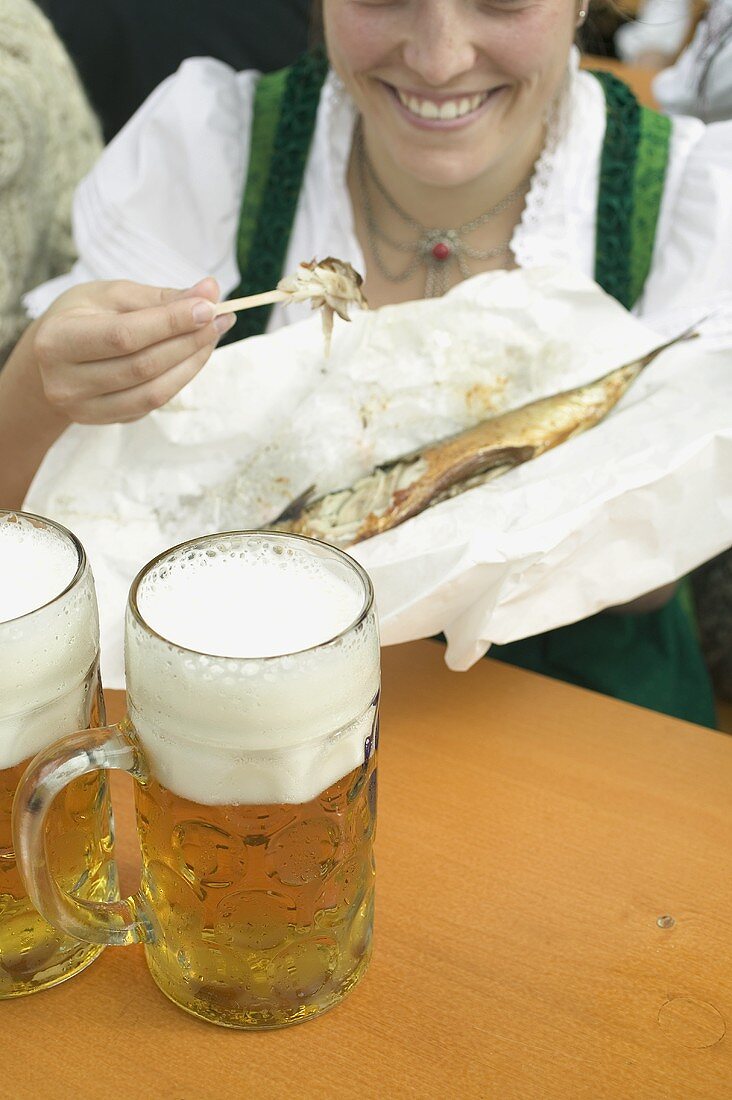 Frau in Tracht isst Steckerlfisch beim Oktoberfest, Mass Bier