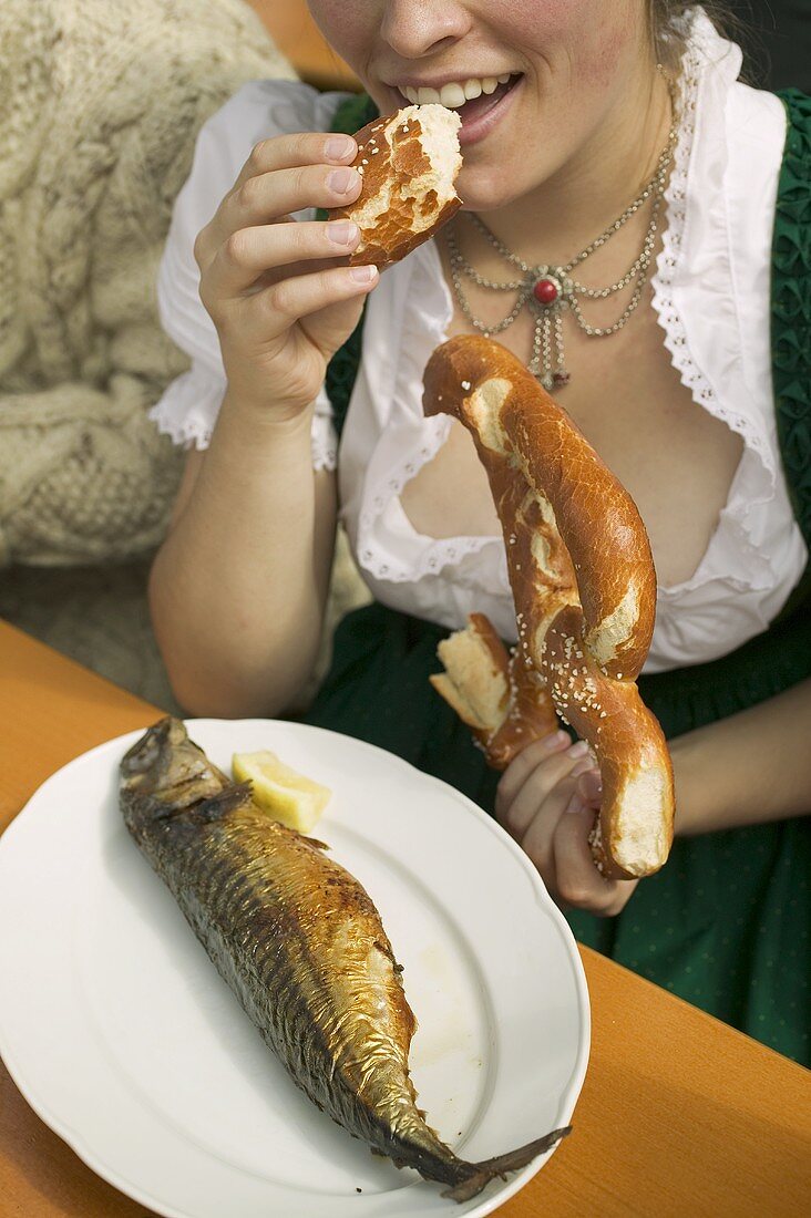 Frau isst Brezel und Steckerlfisch beim Oktoberfest