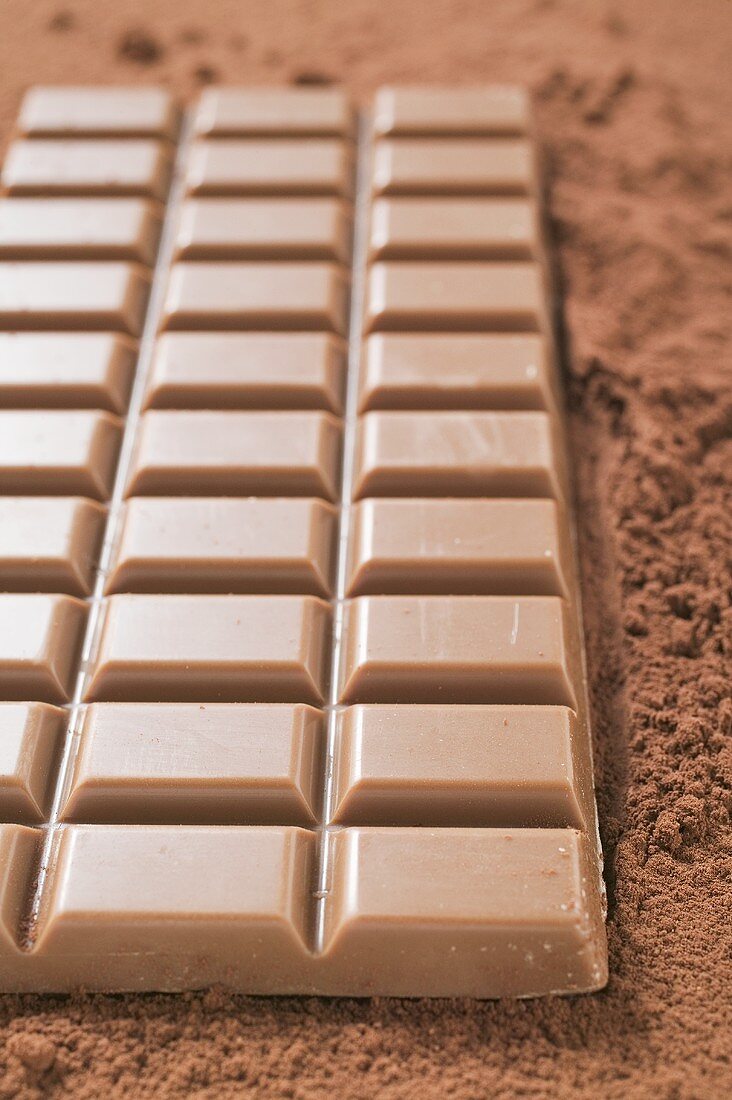 A bar of milk chocolate on cocoa powder