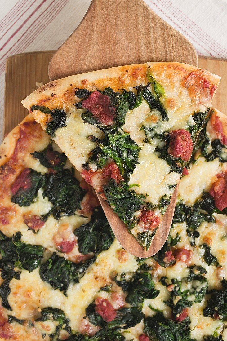 Spinach, tomato and cheese pizza with slice on server
