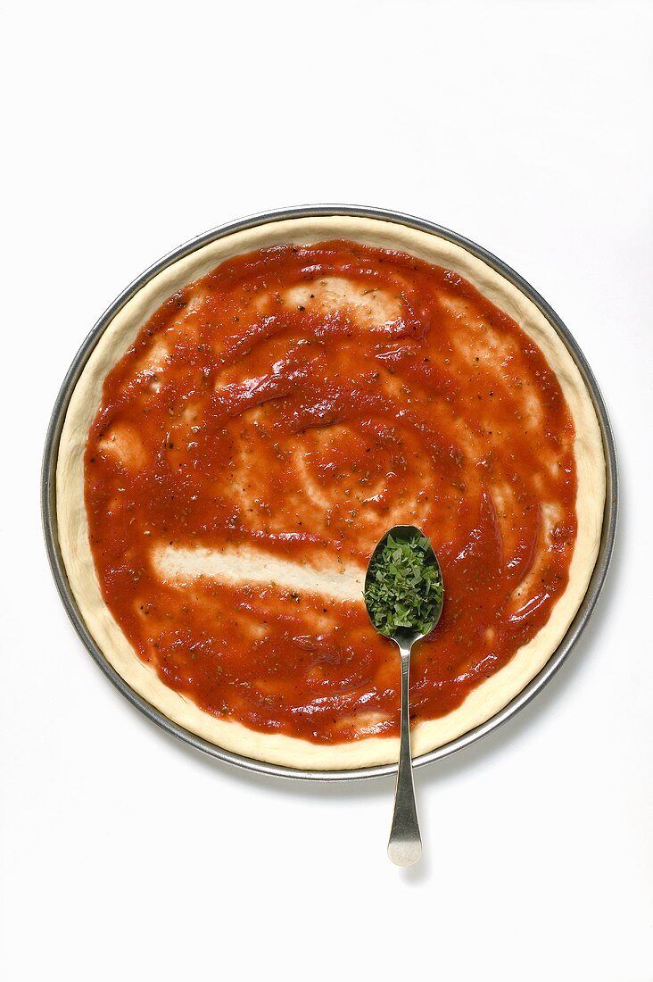 Pizza base with tomato sauce and spoonful of oregano