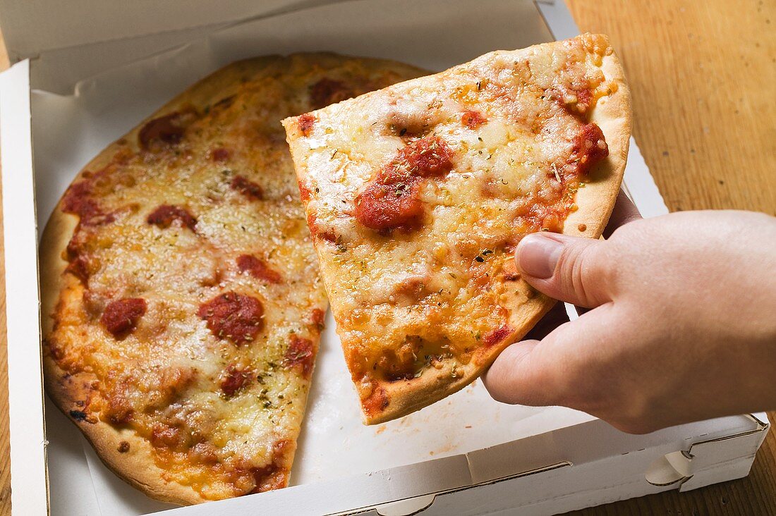 Hand nimmt Stück Pizza Margherita aus Pizzakarton