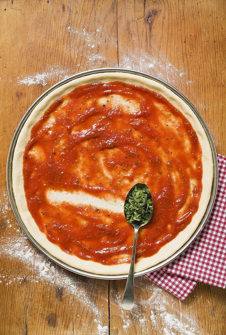 Pizzateig mit Tomatensauce und Löffel Oregano