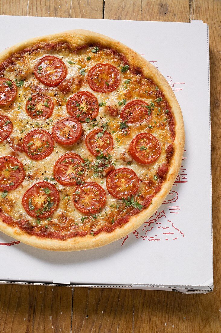 Pizza mit Tomatenscheiben, Käse und Oregano auf Pizzakarton