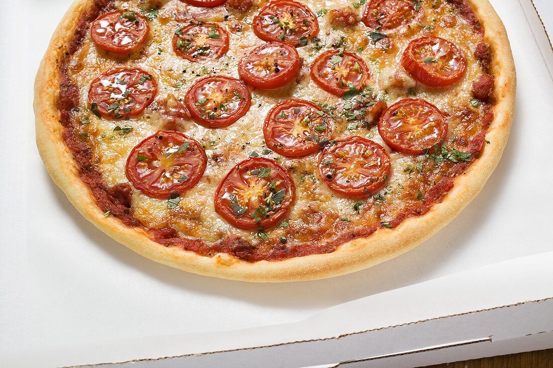 Pizza mit Tomatenscheiben, Käse und Oregano im Pizzakarton