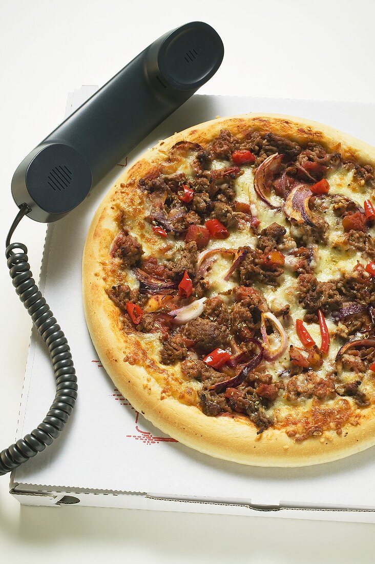 Pizza mit Hackfleisch auf Pizzakarton mit Telefonhörer