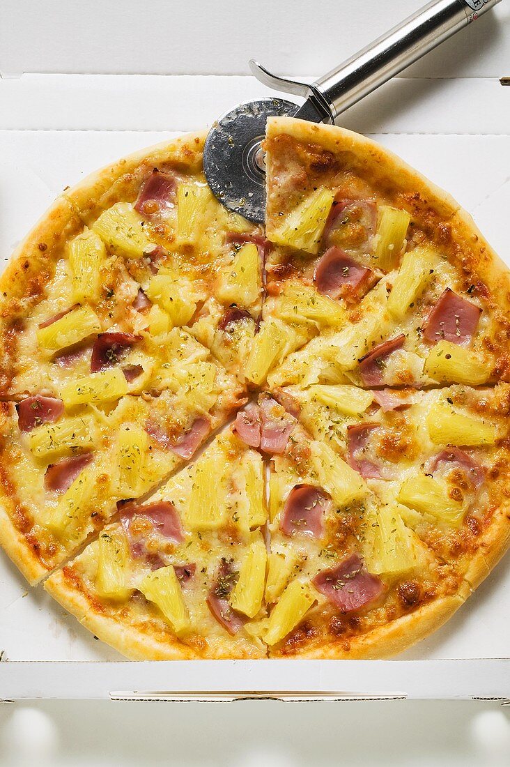 Hawaiian pizza, sliced, in pizza box with pizza cutter