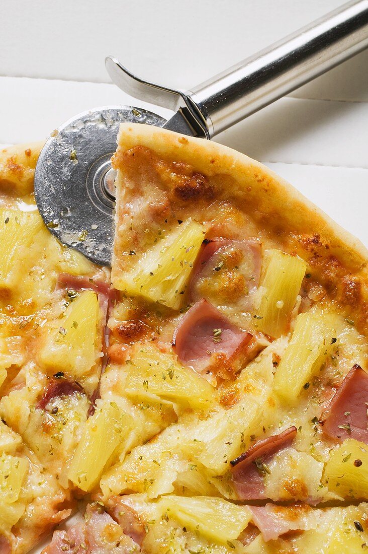 Pizza Hawaii, zerteilt, mit Pizzaschneider im Pizzakarton