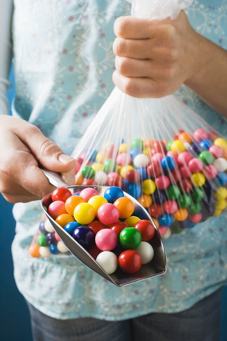 Hände halten Schaufel und Plastiktüte mit Kaugummikugeln