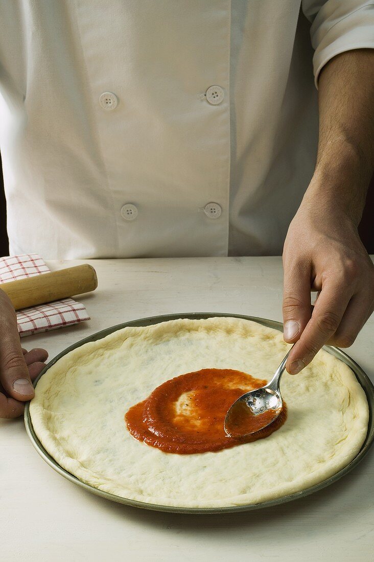 Spreading pizza dough with tomato sauce