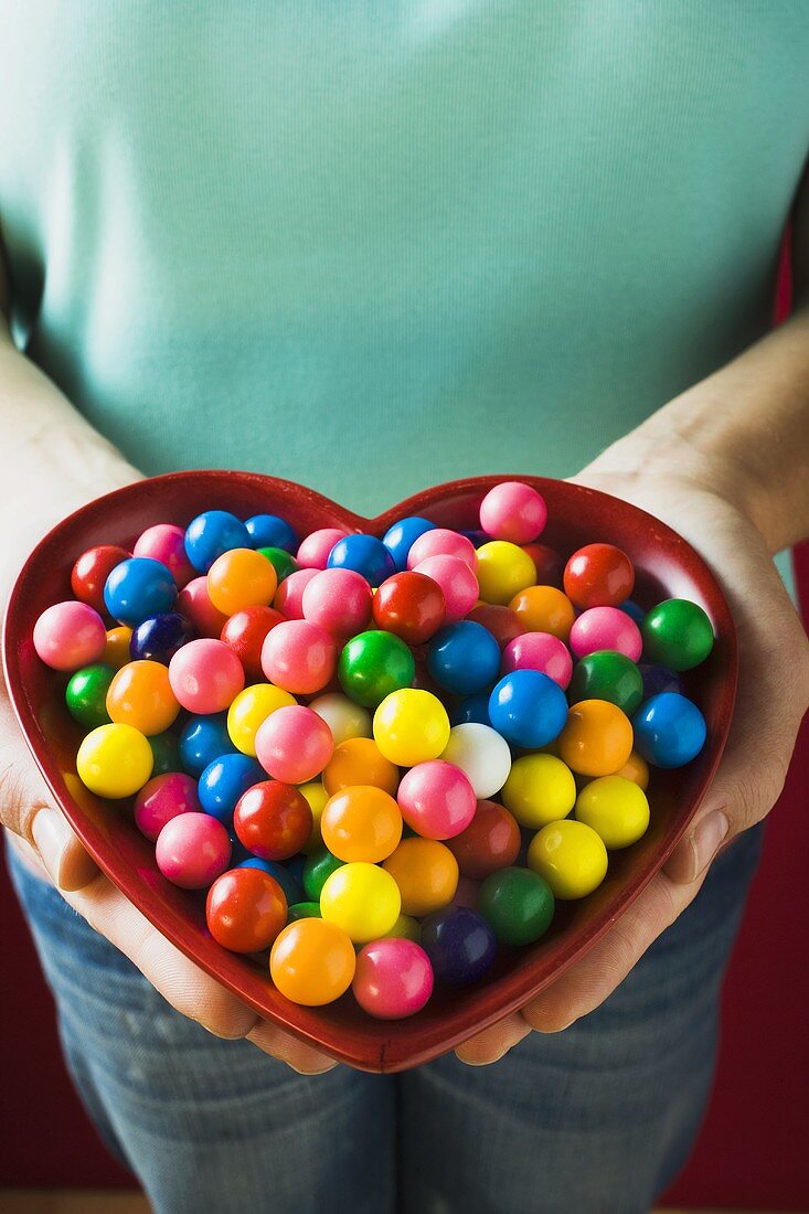 Hands holding a heart-shaped dish of bubble gum balls