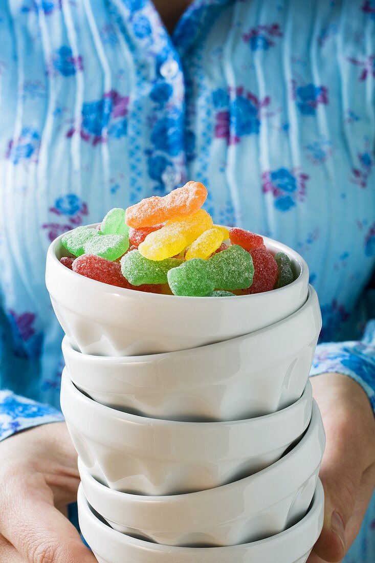 Hands holding pile of bowls with jelly sweets in top bowl