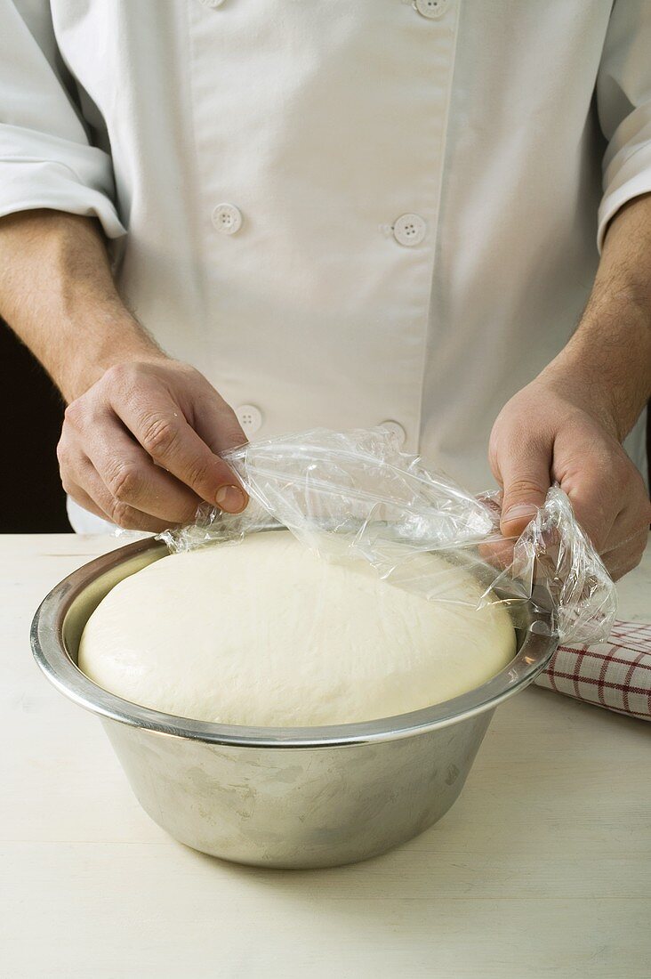 Leaving pizza dough to rest in a bowl (removing clingfilm)