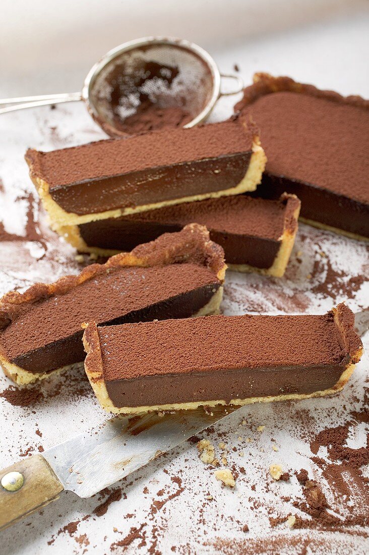 Rectangular chocolate tart with cocoa powder, partly sliced