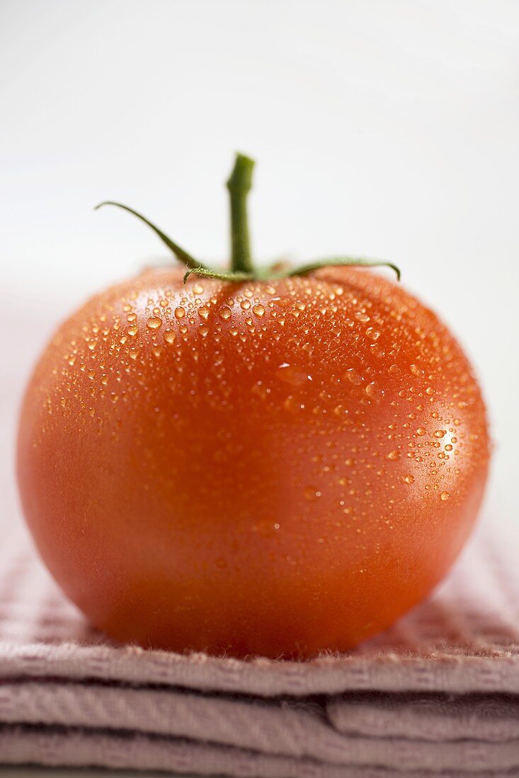 Tomato with drops of water on tea towel