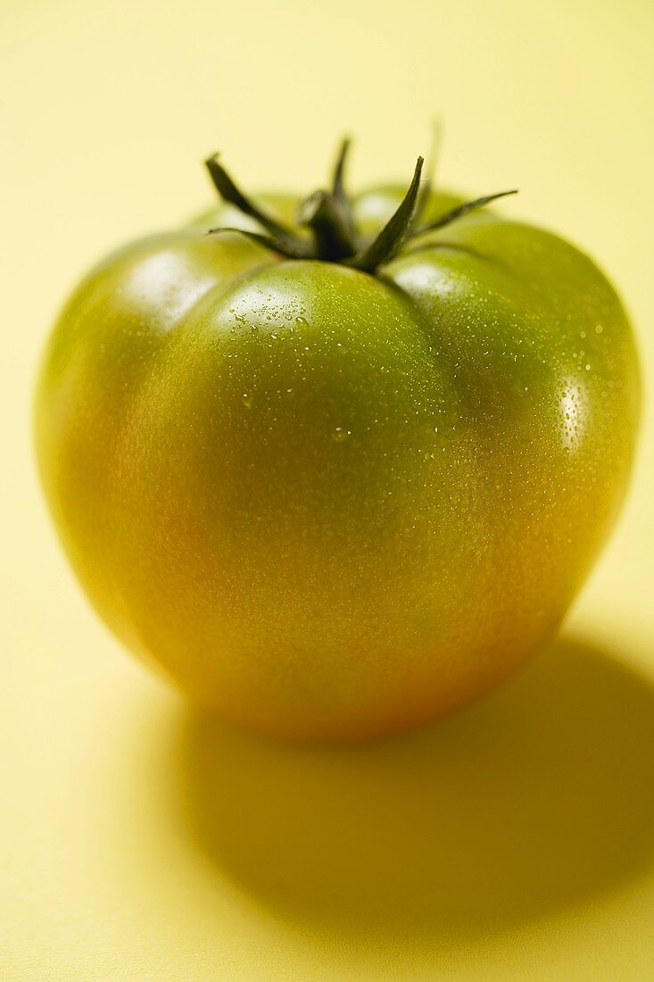 Grüne Tomate auf gelbem Untergrund
