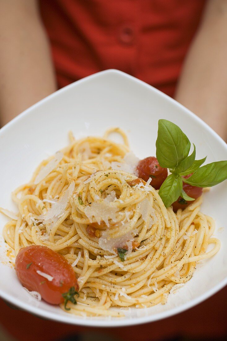 Hands holding plate of spaghetti with Parmesan and basil