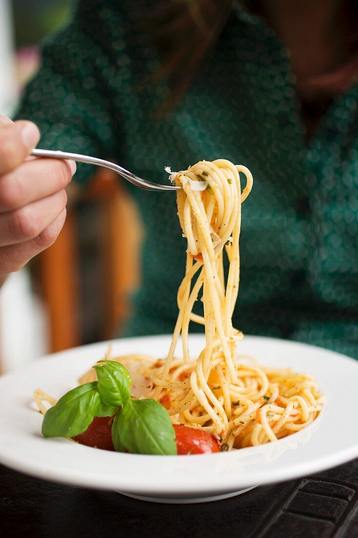 Frau isst Spaghetti mit Tomaten und Basilikum