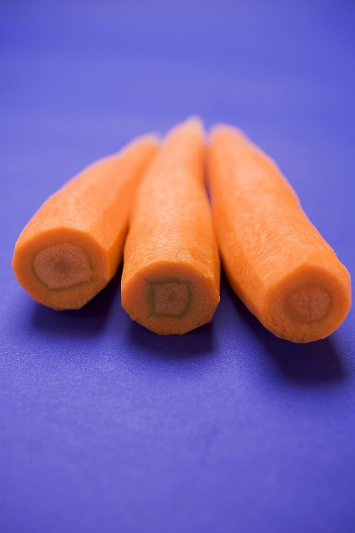 Three peeled carrots on blue background